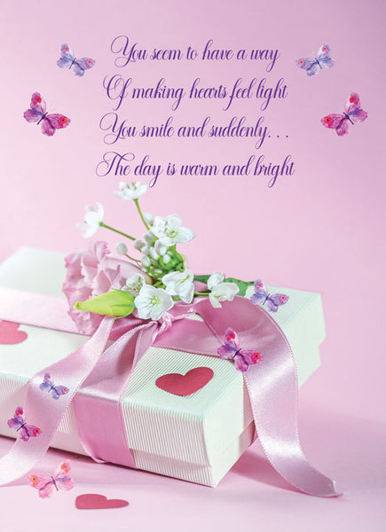 Inside of large pink birthday greeting card featuring a wrapped gift box with a pink ribbon, white flowers, butterflies, and purple cursive text that reads, 'You seem to have a way Of making hearts feel light You smile and suddenly.